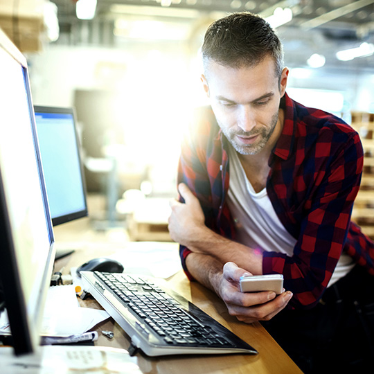 man sitting in front of a laptop checking his phone